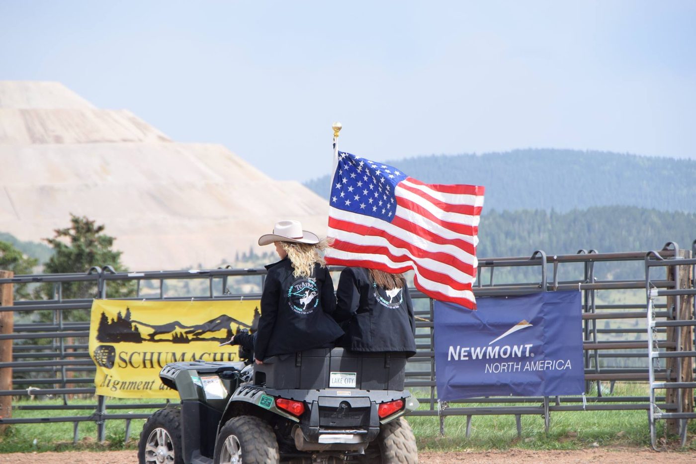 Two Teller County Fair rodeo royalty riders carry the American flag across the arena, the Cripple Creek mine terraces in the distance